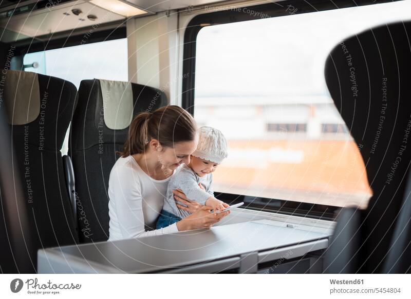 Mother with baby girl traveling by train looking on cell phone travelling mother mommy mothers ma mummy mama mobile phone mobiles mobile phones Cellphone