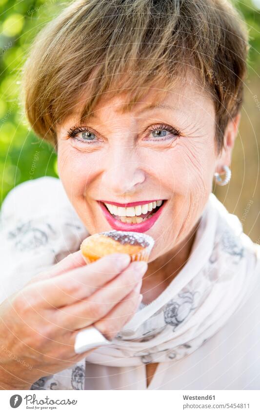 Portrait of smiling senior woman eating a muffin outdoors smile females women muffins senior women elder women elder woman old Adults grown-ups grownups adult