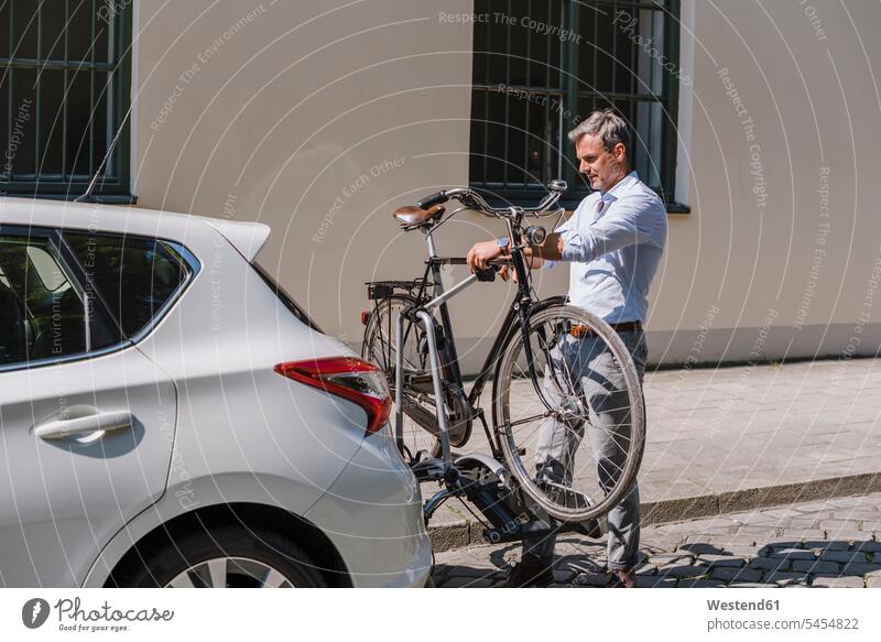Man fixing bicycle on trailer at car man men males bikes bicycles automobile Auto cars motorcars Automobiles city town cities towns Adults grown-ups grownups