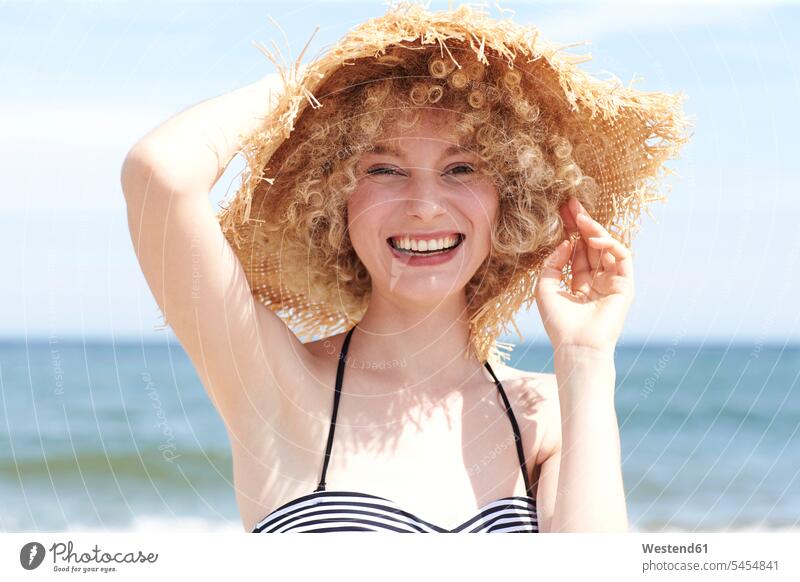 Portrait of laughing young woman wearing straw hat on the beach females women hats portrait portraits Adults grown-ups grownups adult people persons human being