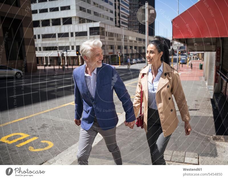 Mature couple walking in the city town cities towns twosomes partnership couples together going on the move on the way on the go on the road holding hands