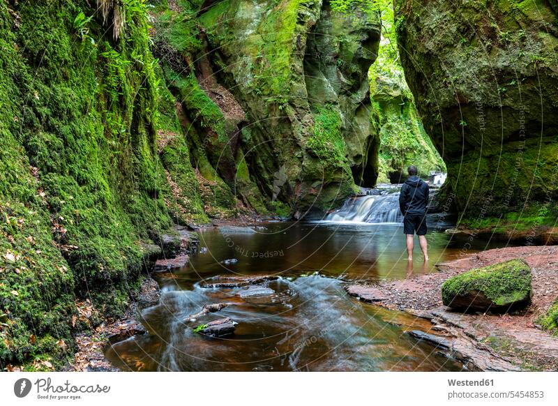 Great Britain, Scotland, Trossachs National Park, Finnich Glen canyon, The Devil's Pulpit, River Carnock Burn, male tourist standing in water rock face