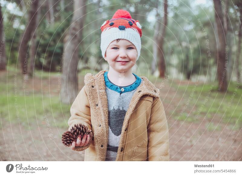 Portrait of boy wearing wooly hat holding pine cones in forest smiling smile Pine Cone Pine Cones Pinecones woolly hat Wooly Hat Knit-Hat Knit Hats wool cap