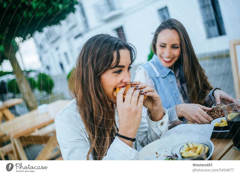 Two women eating Hamburgers in a street restaurant woman females hamburger Adults grown-ups grownups adult people persons human being humans human beings Meat