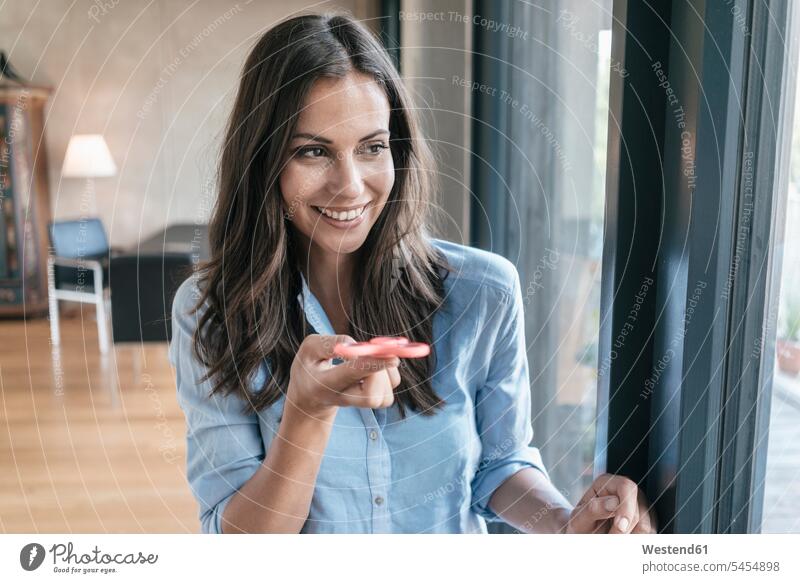 Smiling woman with fidget spinner at the window standing smiling smile relaxed relaxation females women music relaxing Adults grown-ups grownups adult people