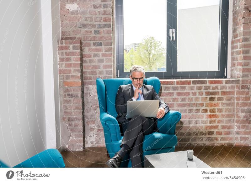 Mature businessman sitting in arm chair, using laptop Seated Laptop Computers laptops notebook armchair Arm Chairs armchairs working At Work window windows