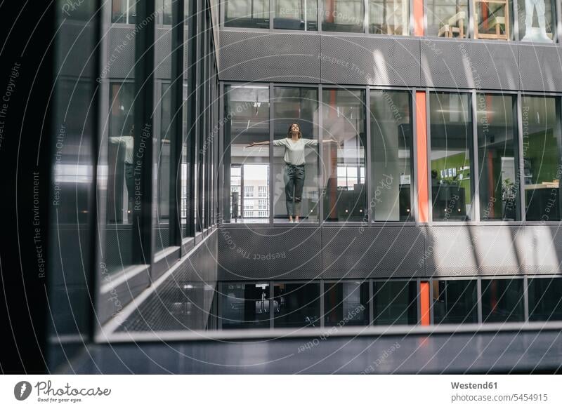 Woman standing at office window, with arms outstretched businesswoman businesswomen business woman business women glass pane glass panes offices office room