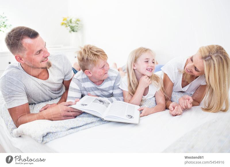 Family lying in bed reading book together smiling smile family families books beds people persons human being humans human beings home at home Care caring care