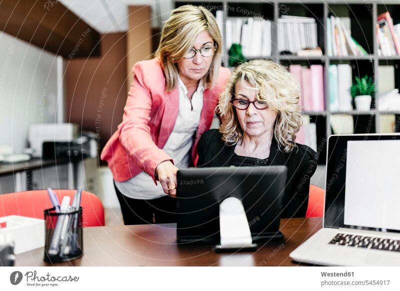 Two businesswomen using laptop at desk in office offices office room office rooms businesswoman business woman business women Laptop Computers laptops notebook