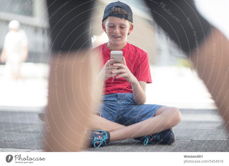 Boy using smart phone, sitting on skateboard mobile phone mobiles mobile phones Cellphone cell phone cell phones reading texting sending Seated Skate Board