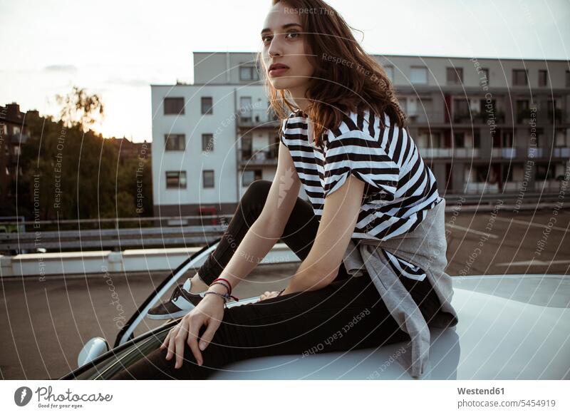Serious young woman sitting on car roof automobile Auto cars motorcars Automobiles serious earnest Seriousness austere females women Roof Seated motor vehicle