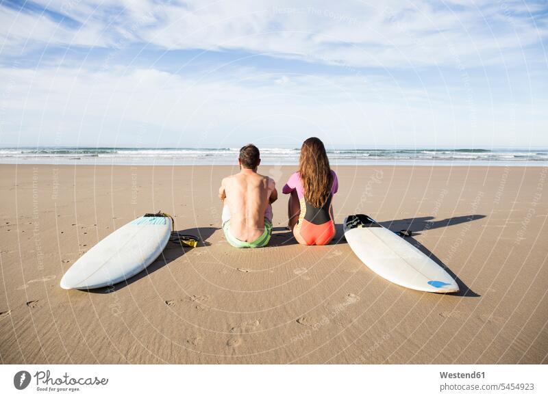 Couple with surfboards sitting on the beach Seated beaches couple twosomes partnership couples surfer surfers surfing surf ride surf riding Surfboarding