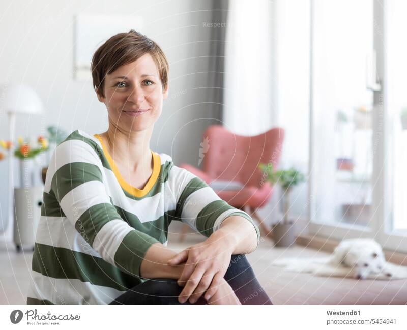 Portrait of smiling woman sitting on the floor in the living room portrait portraits females women Adults grown-ups grownups adult people persons human being