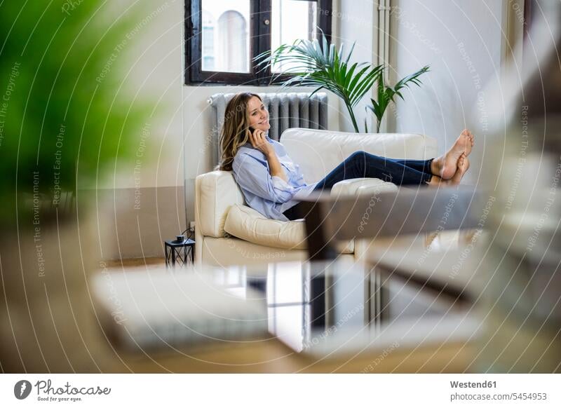 Smiling woman on couch at home on the phone call telephoning On The Telephone calling mobile phone mobiles mobile phones Cellphone cell phone cell phones