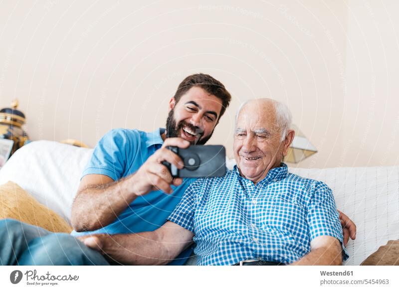 Portrait of adult grandson and his grandfather taking selfie with smartphone at home Selfie Selfies grandsons senior men senior man elder man elder men