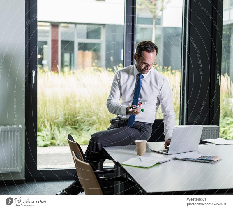 Businessman with atomic model using laptop in his office Business man Businessmen Business men offices office room office rooms business people businesspeople