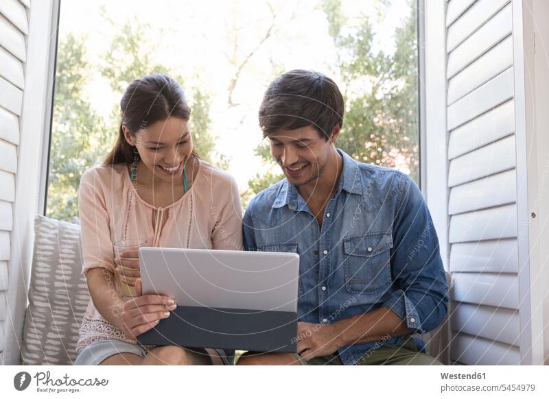 Smiling young couple sitting on windowsill sharing tablet relaxed relaxation smiling smile twosomes partnership couples Seated digitizer Tablet Computer
