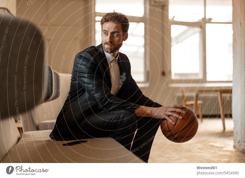 Portrait of young businessman with basketball sitting on the couch in a loft men males Businessman Business man Businessmen Business men Adults grown-ups