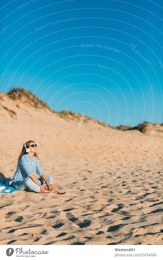 Portugal, Aveiro, woman sitting near beach dune listening music with headphones beach dunes females women sand sandy headset hearing Seated sand dune sand dunes
