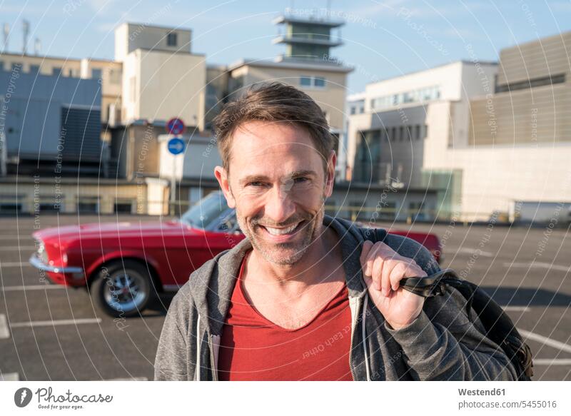 Portrait of smiling mature man in front of his sports car on parking level portrait portraits men males Adults grown-ups grownups adult people persons