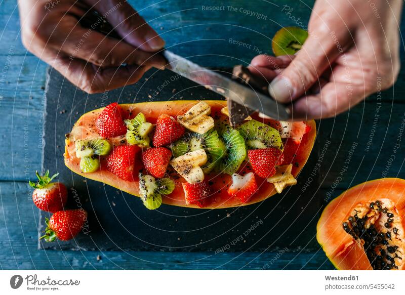 Close-up of man's hands cutting chocolate over half papaya garnished with pieces of banana, kiwi and strawberries Papaya Pawpaw Papayas Pawpaws preparation