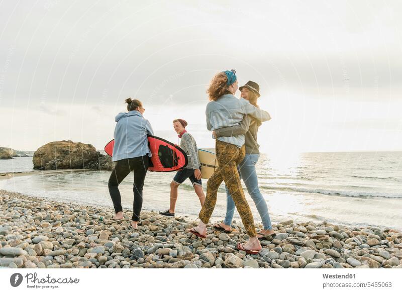 Happy friends with surfboards walking on stony beach happiness happy beaches surfer surfers friendship surfing surf ride surf riding Surfboarding water sports
