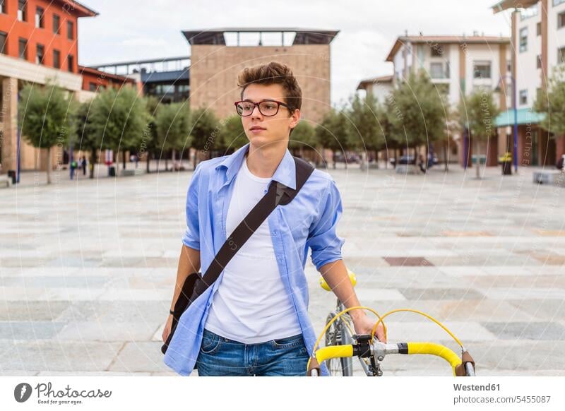 Portrait of young man pushing his bike portrait portraits men males Adults grown-ups grownups adult people persons human being humans human beings bicycle bikes