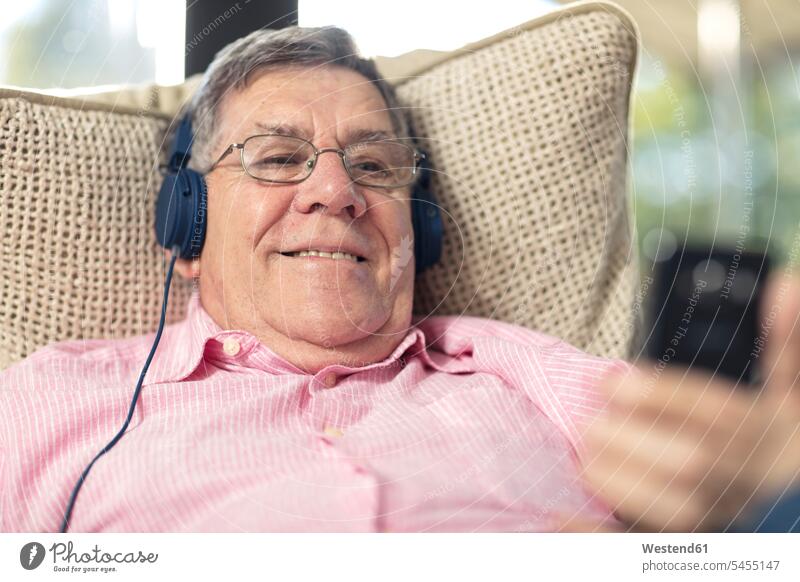 Smiling senior man wearing headphones listening to music at home smiling smile men males hearing couch settee sofa sofas couches settees headset senior men