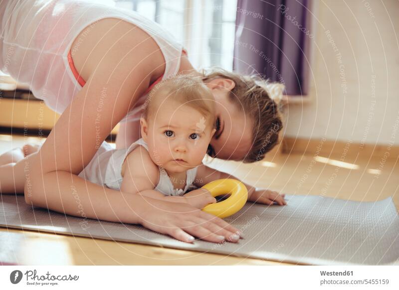 Mother kissing her baby while working out on a yoga mat exercising exercise training practising infants nurselings babies kisses mother mommy mothers mummy mama
