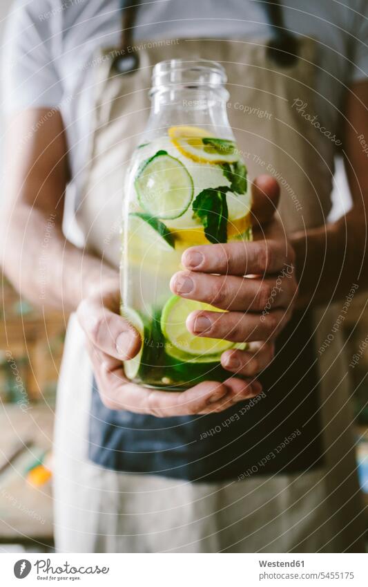 Man's hands holding glass bottle of infused water with lemon, lime, mint leaves and ice cubes human hand human hands people persons human being humans