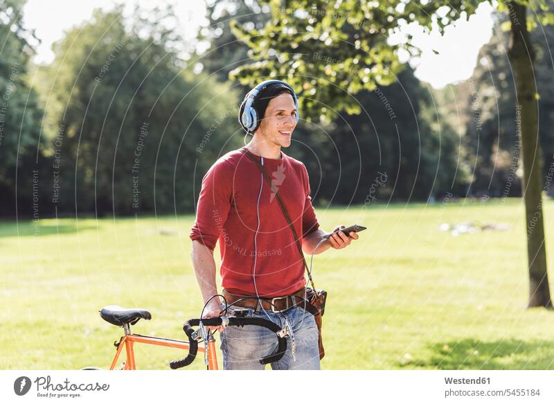 Laughing man with racing cycle listening music with headphones in a park men males parks Adults grown-ups grownups adult people persons human being humans