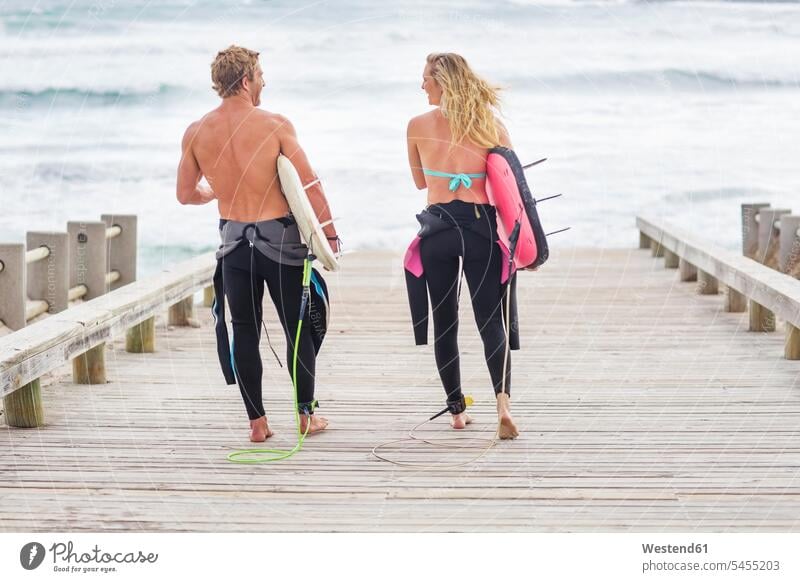 Couple walking to beach with surfboards beaches surfing surf ride surf riding Surfboarding carrying going couple twosomes partnership couples water sports