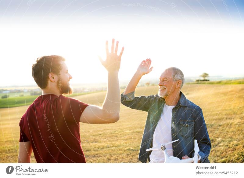Senior father and his adult son with drone on a field quadcopter quadrotor helicopter Quadcopters High Five high fiving Hi-Five high-fiving High-Five drones pa