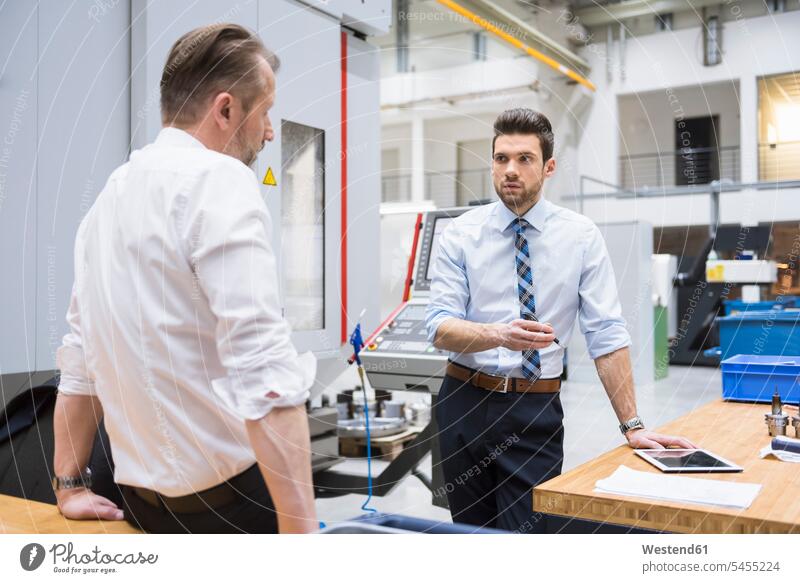 Two businessmen at table in factory shop floor discussing colleagues Businessman Business man Businessmen Business men factories business people businesspeople