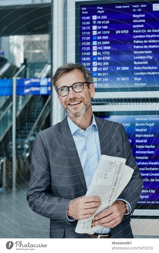 Smiling businessman with newspaper at timetable at the airport terminal airports Businessman Business man Businessmen Business men smiling smile transportation