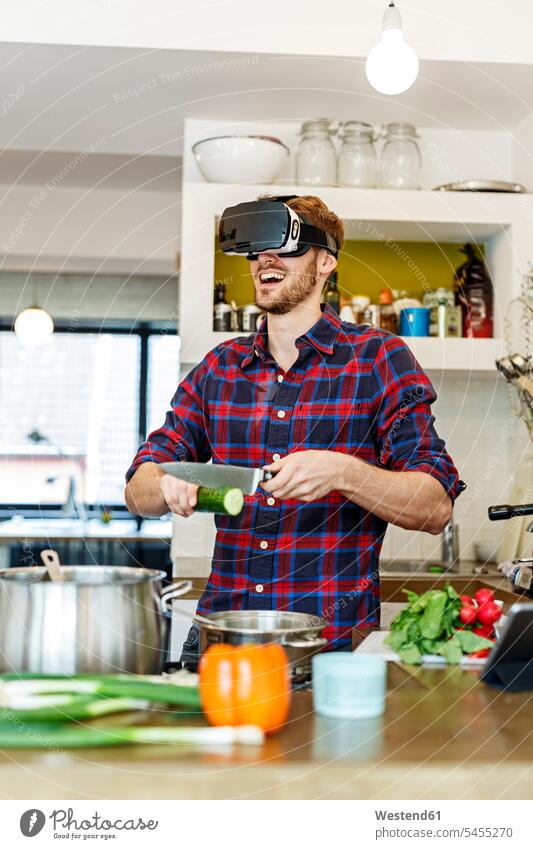 Happy young man wearing VR glasses cooking in kitchen virtual reality happiness happy specs Eye Glasses spectacles Eyeglasses men males Adults grown-ups