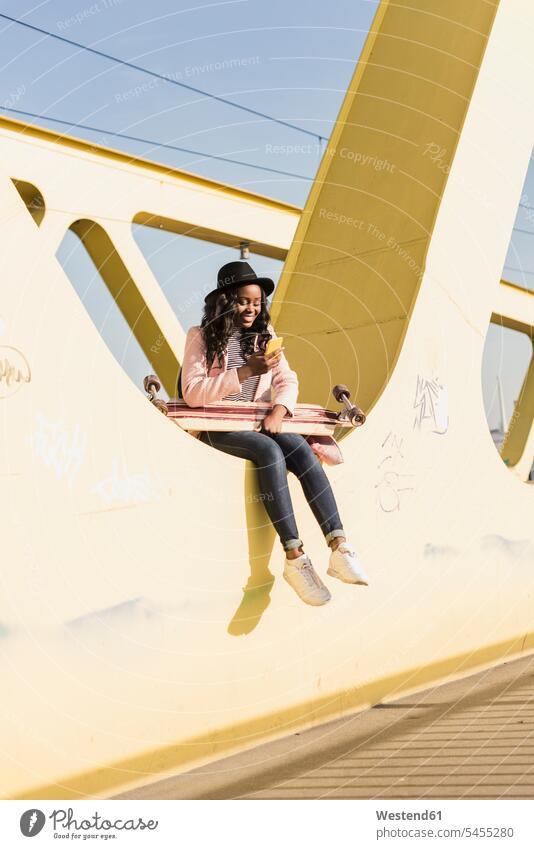 Young woman sitting on bridge using smartphone young Seated females women bridges Adults grown-ups grownups adult people persons human being humans human beings