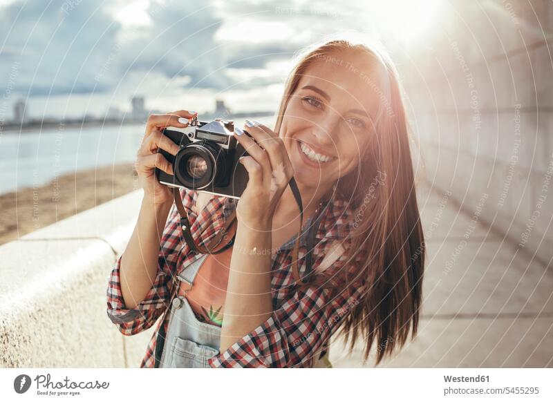 Smiling young woman with a camera at the riverside females women cameras portrait portraits smiling smile River Rivers Adults grown-ups grownups adult people