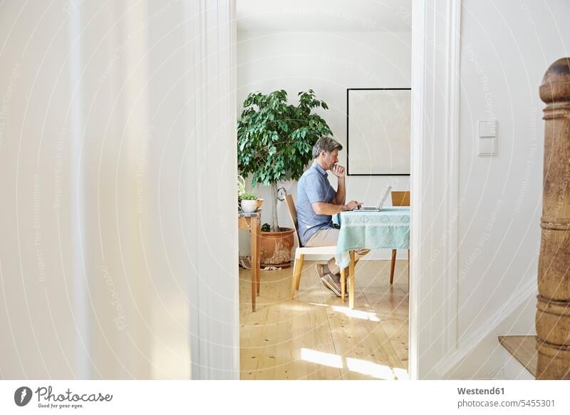Mature man sitting in his dining room, using laptop Laptop Computers laptops notebook men males home ownership private owned home Internet The Internet