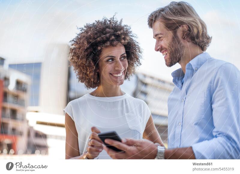 Businessman and woman having a meeting outdoors, using smartphone colleagues discussing discussion casual conference on the move on the way on the go