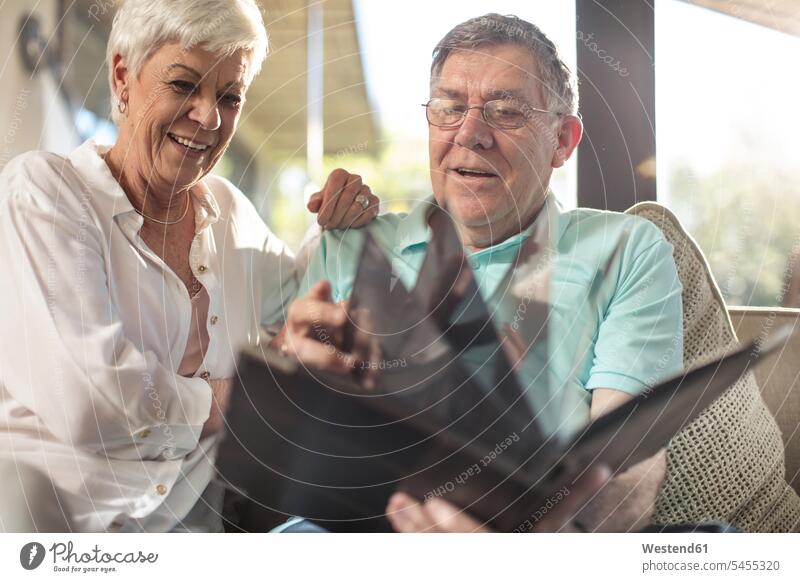 Happy senior couple sitting on couch looking at photo album settee sofa sofas couches settees eyeing happiness happy home at home twosomes partnership couples