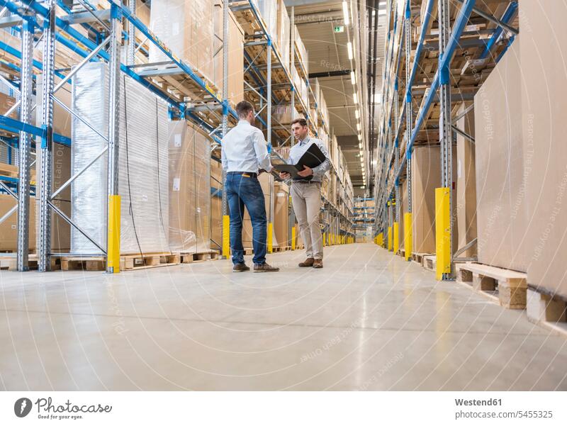 Two men with folder talking in factory warehouse speaking working At Work colleagues man males storehouse storage Adults grown-ups grownups adult people persons