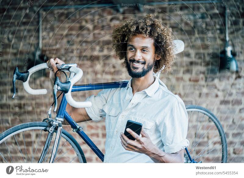 Smiling young man with bicycle and cell phone bikes bicycles smiling smile men males mobile phone mobiles mobile phones Cellphone cell phones Adults grown-ups