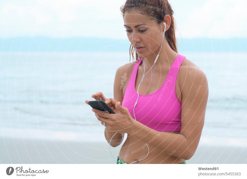 Woman listening music from her smartphone Listening Music Smartphone iPhone Smartphones fit beach beaches sportive sporting sporty athletic woman females women