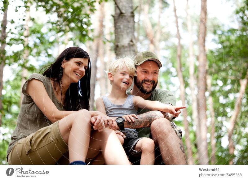 Happy family with son sitting in forest laughing Laughter pointing point at pointing at show showing families woods forests sons manchild manchildren positive