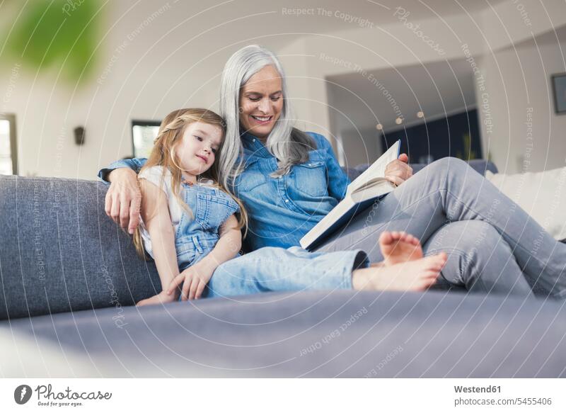 Grandmother and granddaughter sitting on couch, reading together learning Seated granddaughters settee sofa sofas couches settees grandmother grandmas