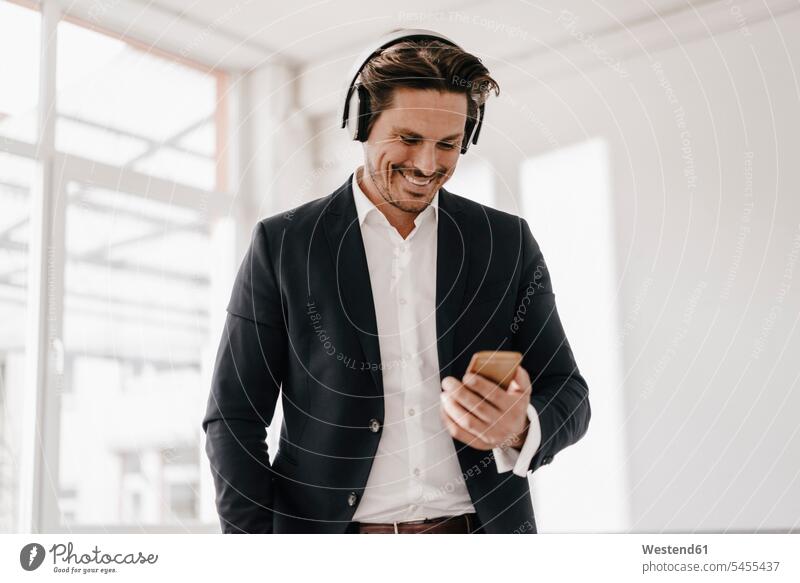 Smiling businessman with cell phone and headphones relaxed relaxation men males mobile phone mobiles mobile phones Cellphone cell phones hearing headset