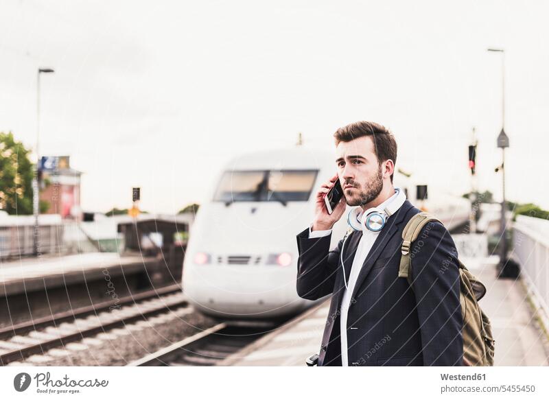 Young man using cell phone on platform as train coming in journey travelling Journeys voyage on the phone call telephoning On The Telephone calling men males