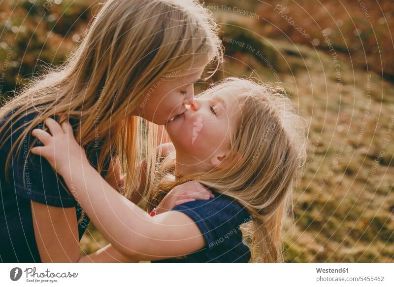 Two cute blond sisters kissing outdoors kisses embracing embrace Embracement hug hugging girl females girls siblings brother and sister brothers and sisters