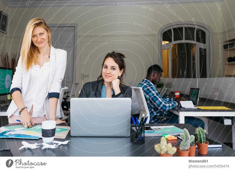 Young businesswomen working together, using laptop, colleague sitting in background Seated Female Colleague team Laptop Computers laptops notebook businesswoman